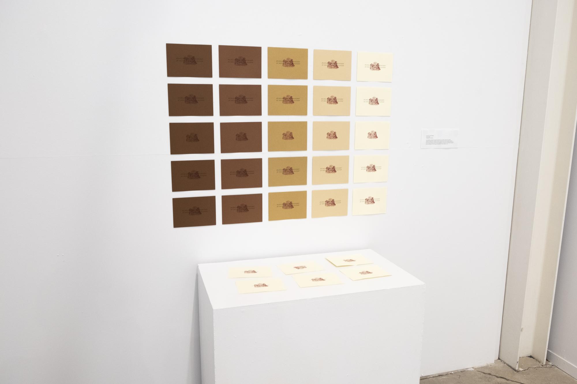 angle view of the prints arranged in a grid on the wall and some prints on a plinth in front of the wall