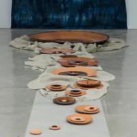 ceramic dishes varying in size sit on a gray concrete floor leading towards a wall with a large blue textile hanging on it