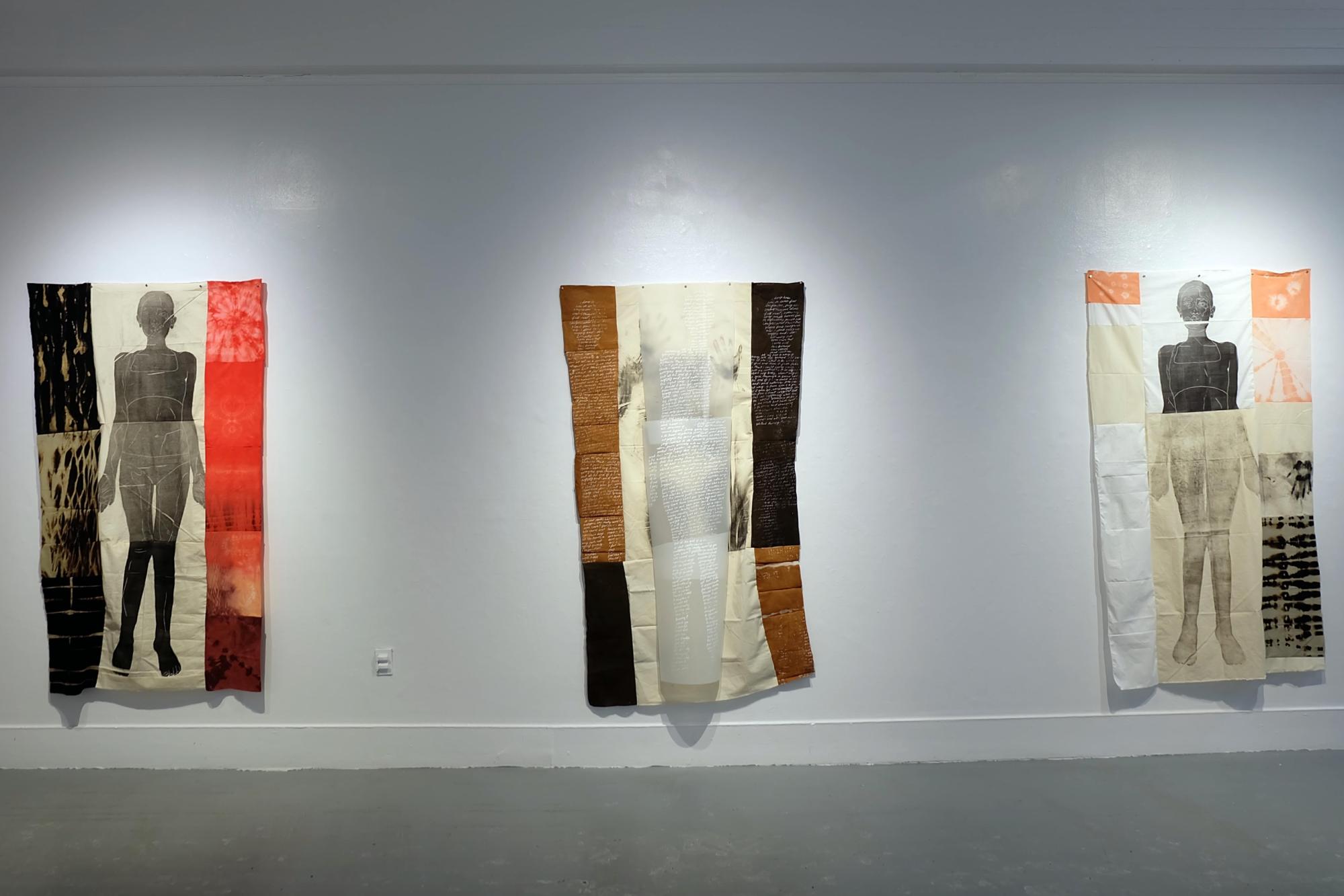 Three 6 foot tall prints of black bodies on quilted fabric hang in a gallery space