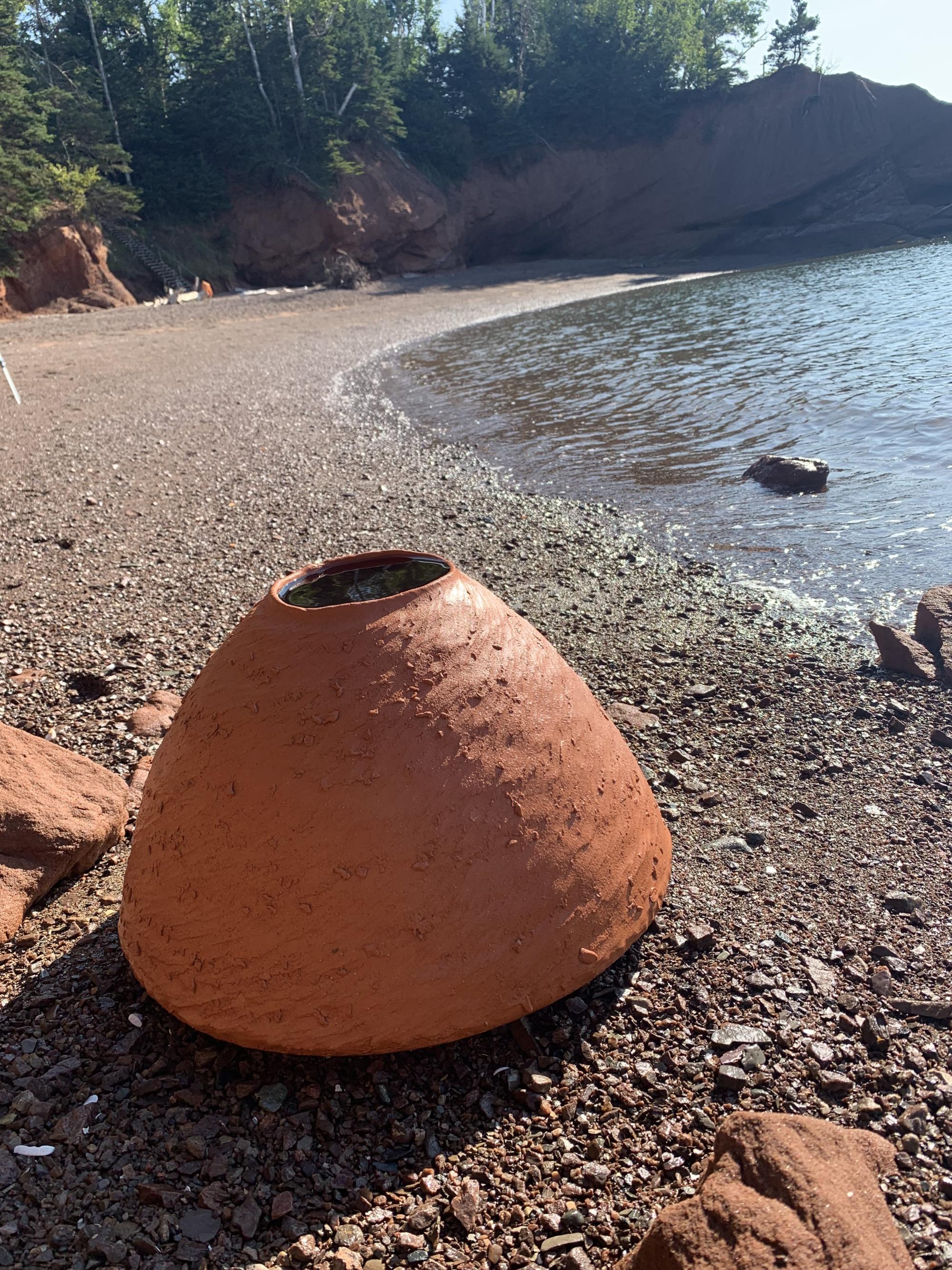 A clay vessel sits on a rock beach