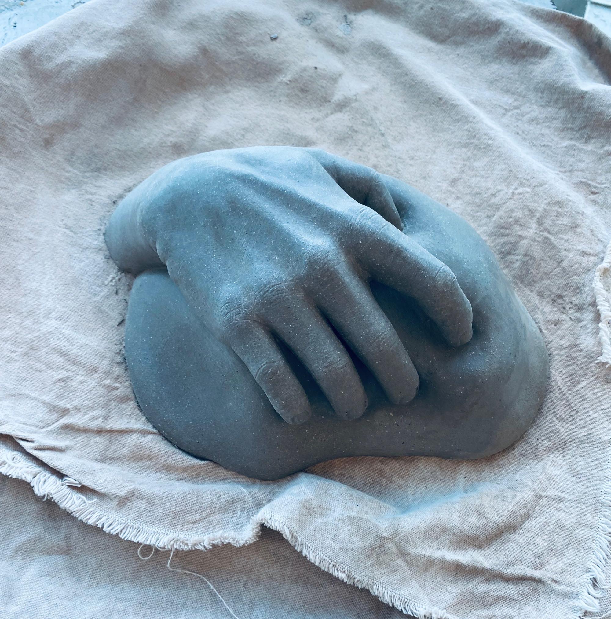Medium dark gray clay hand grasping onto medium dark gray fleshy-looking figure.
