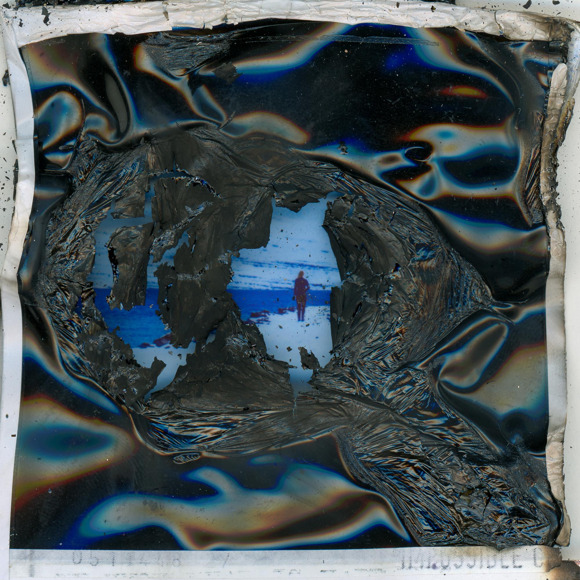Distorted and damaged photograph, with predominantly black areas, as well as medium dark blue, orange and white.