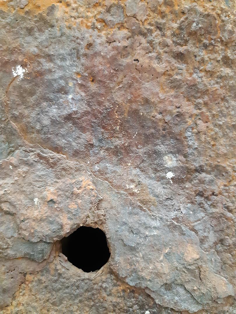 An uneven and rust-covered surface punctured by a single hole