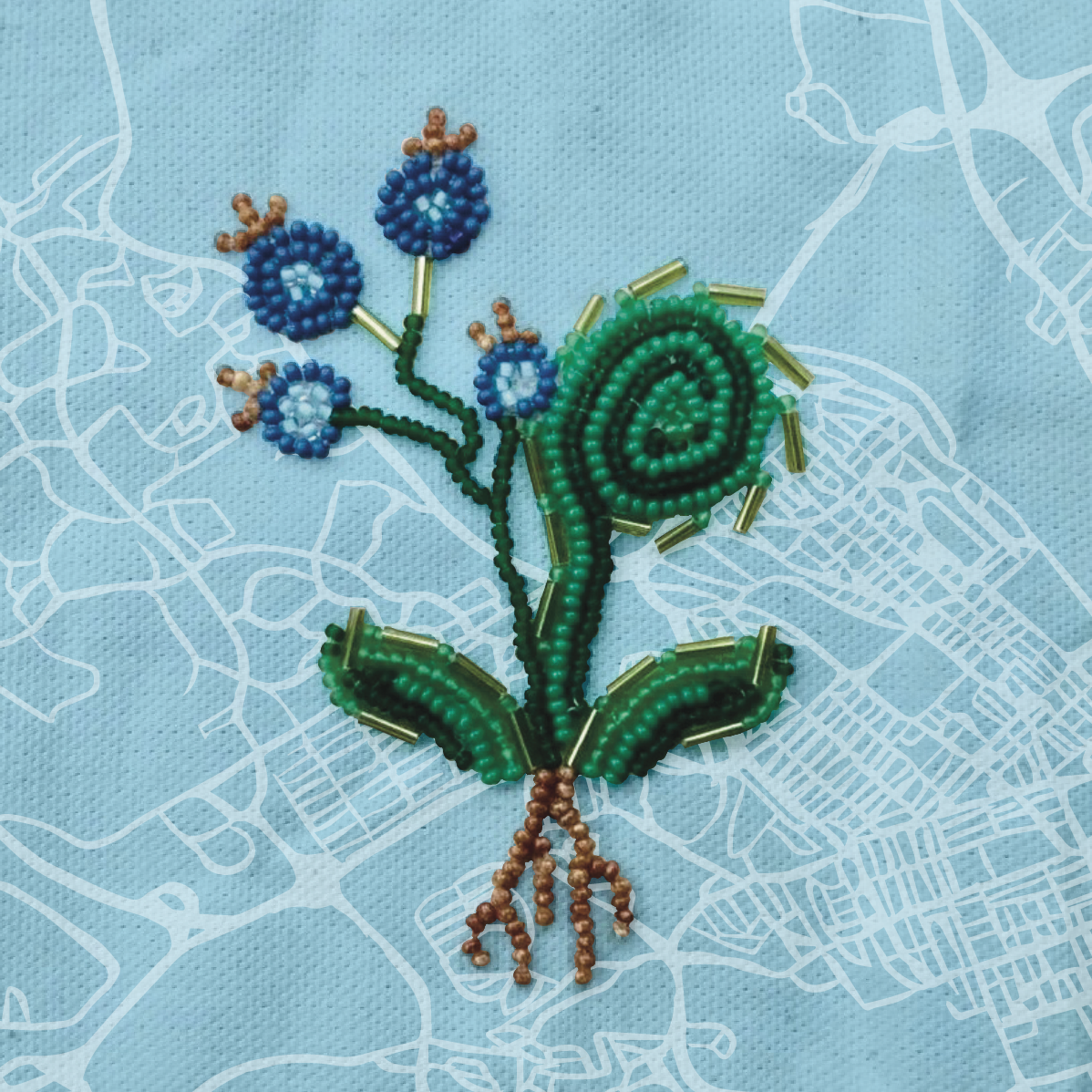 Photograph of green fiddlehead and blueberry design created with small glass beads in foreground. Light blue background with canvas texture and white, low-opacity graphic linework of Halifax city street grid.