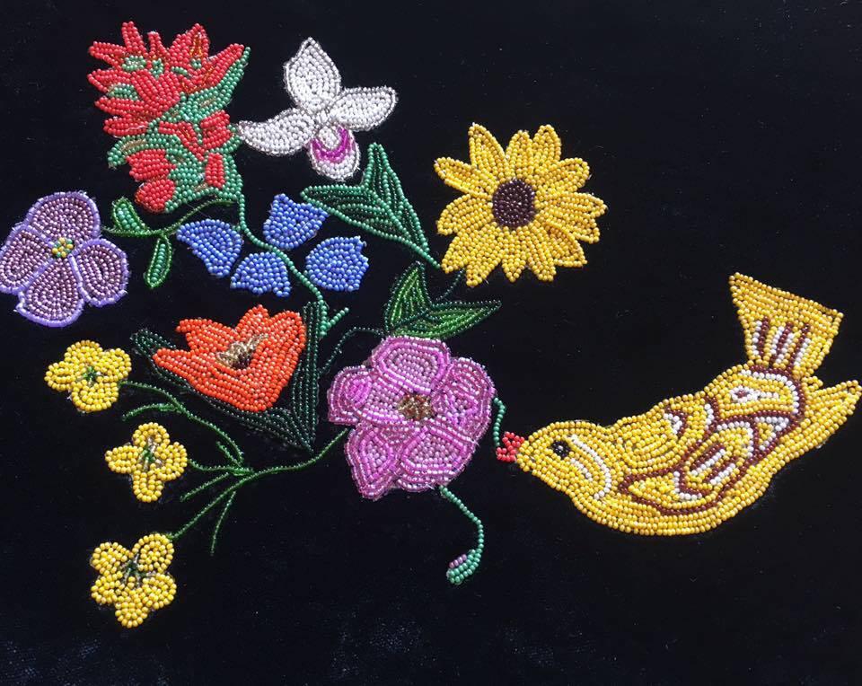 Florals and bird design made up of many small, colorful glass beads on a black background. Beaded flowers are yellow, red, blue, and purple and bird is bright yellow