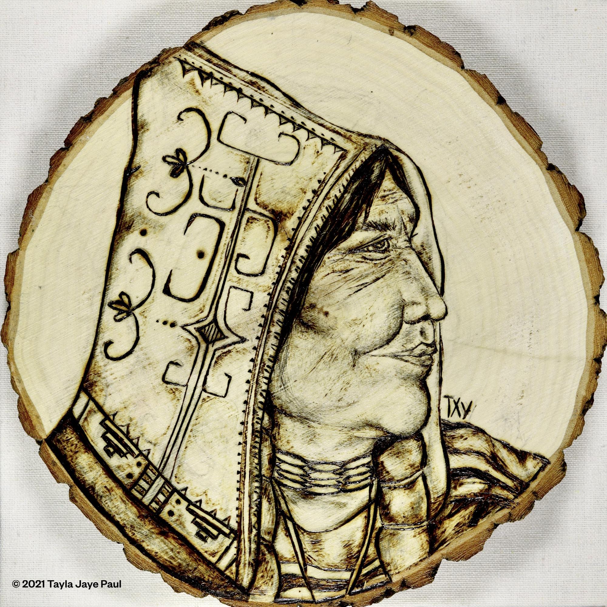 Circular wooden disk with woodburned illustration of the side profile of an older Mi'kmaw woman looking into the distance to the right. She is wearing a peaked cap with traditional double-curve designs 