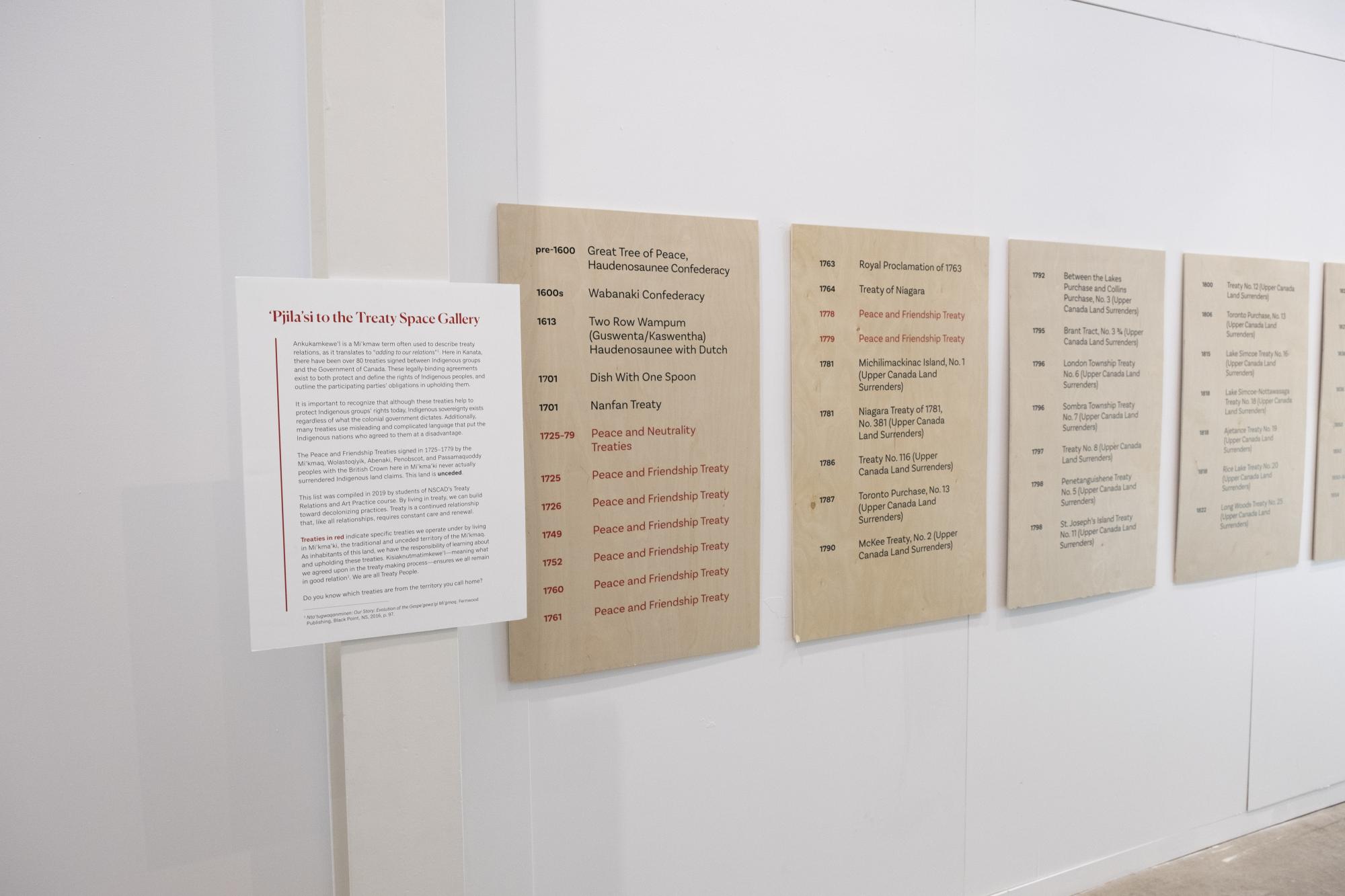 photograph of wooden boards mounted on white wall with black and red vinyl text listing the treaties in North America