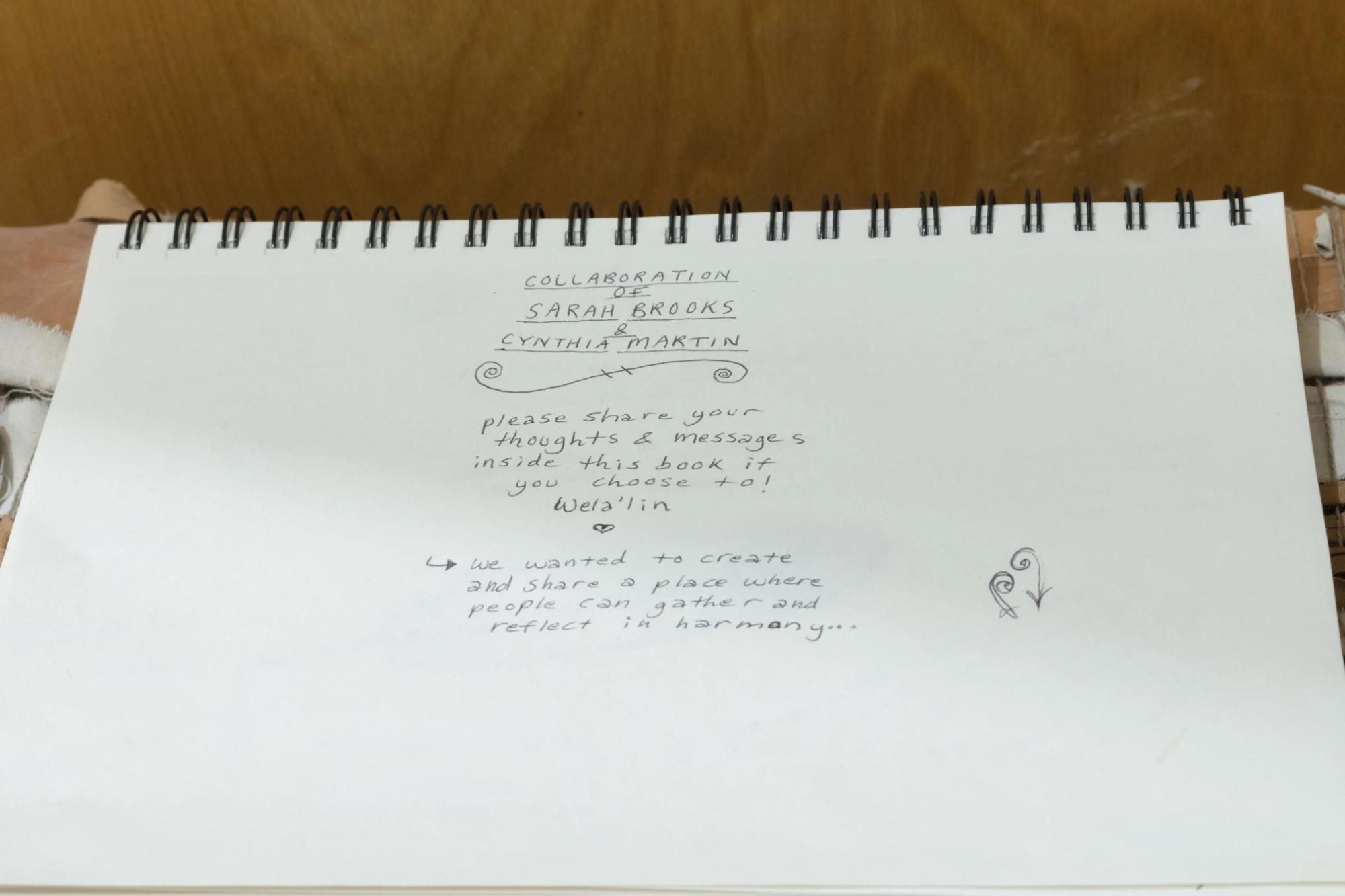 closeup of the guest book reading "collaboration of Sarah Brooks and Cynthia Martin. Please share your thoughts and messages inside this book if you choose to! Wela'lin. We wanted to create and share a place where people can gather and reflect in harmony..."