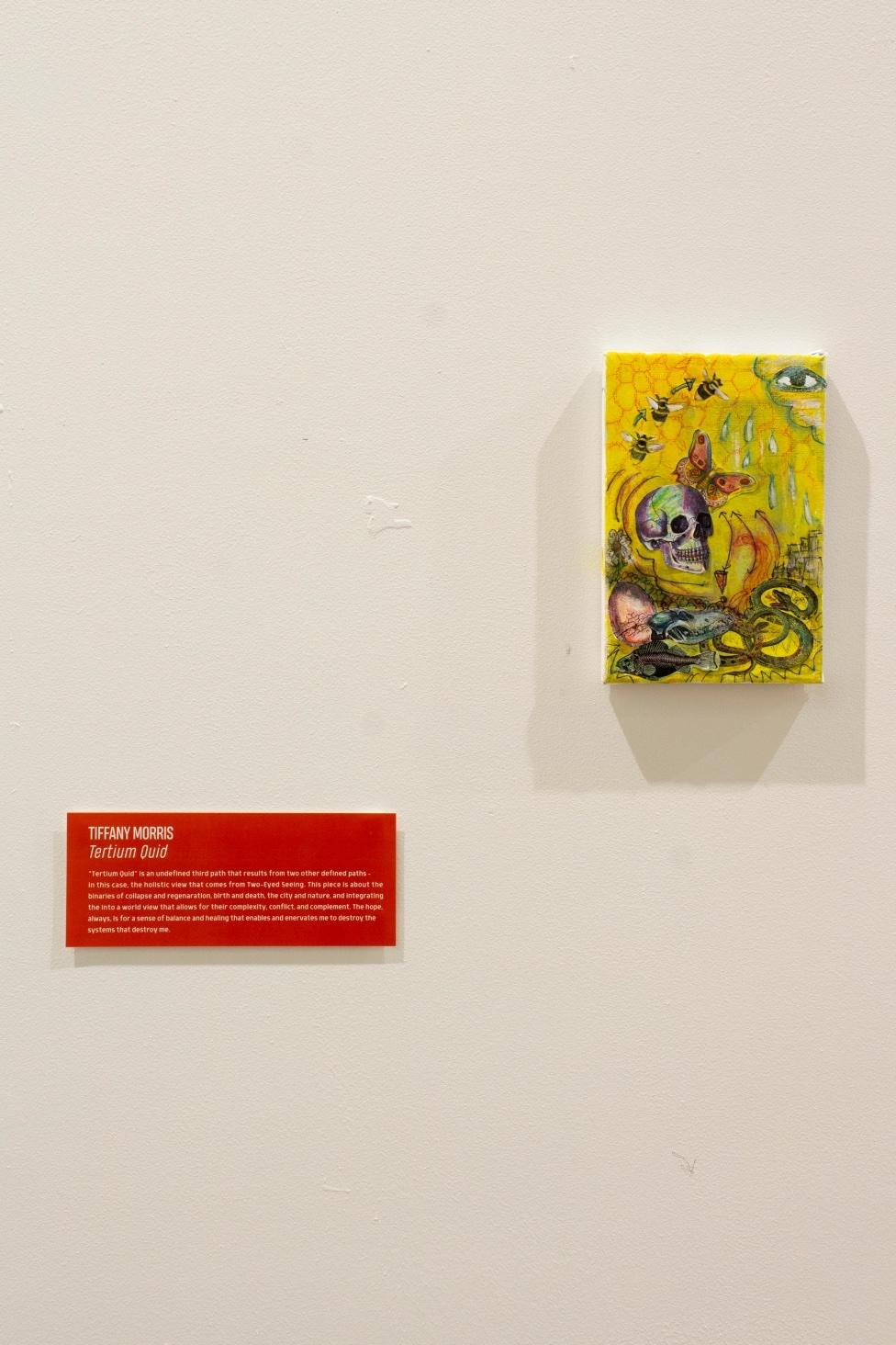 a small yellow painting on the wall next to a red didactic panel