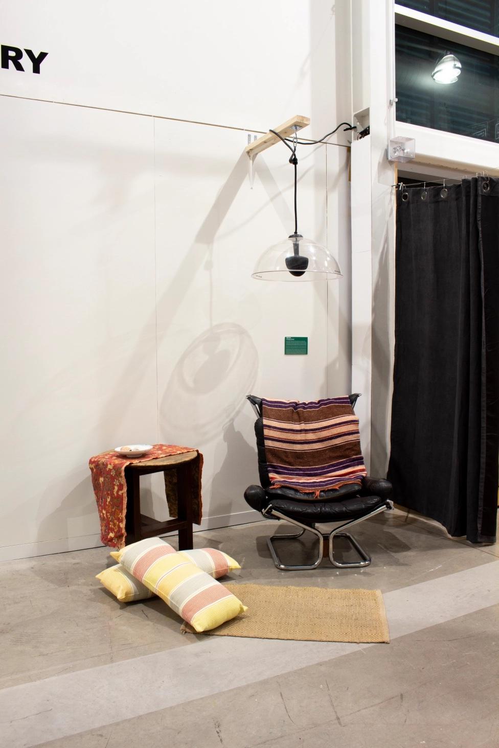 a lounge change and side table with pillows arranged under a parabolic speaker hanging above it