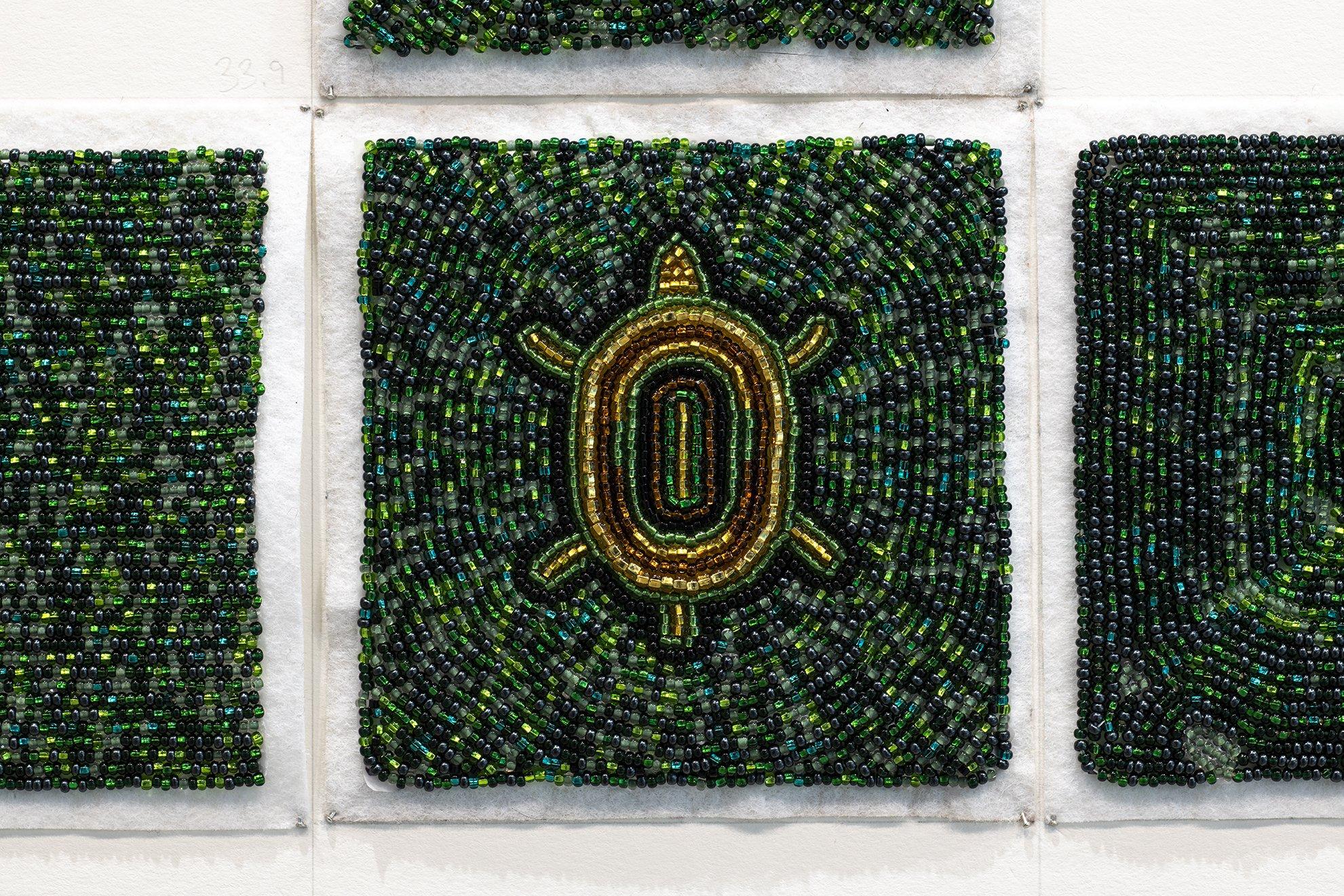 closeup of beaded square made up of small glass green seed beads with brown and gold beads in the centre in the shape of a turtle