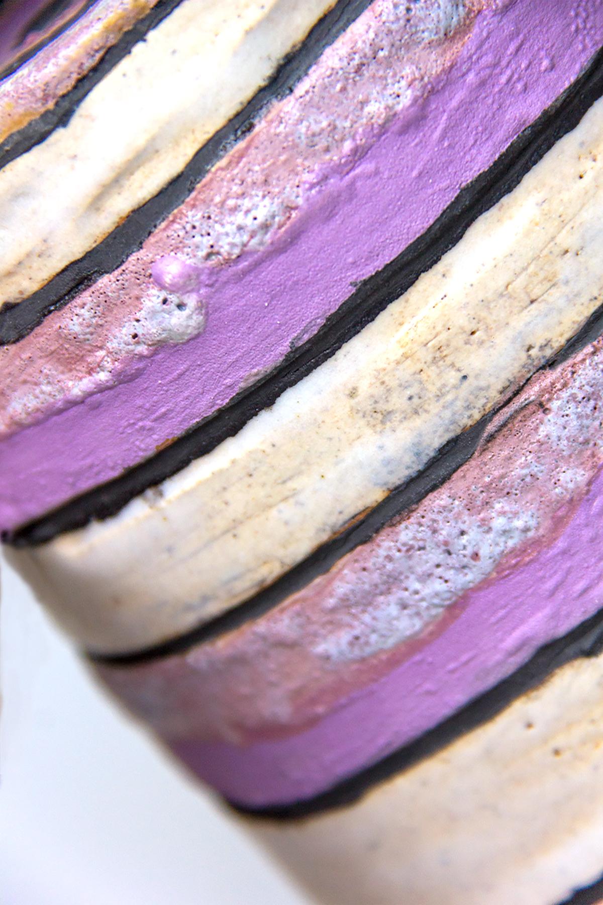 A close-up of a ceramic vessel with purple, black and off-white diagonal glaze stripes extending upwards from left to right
