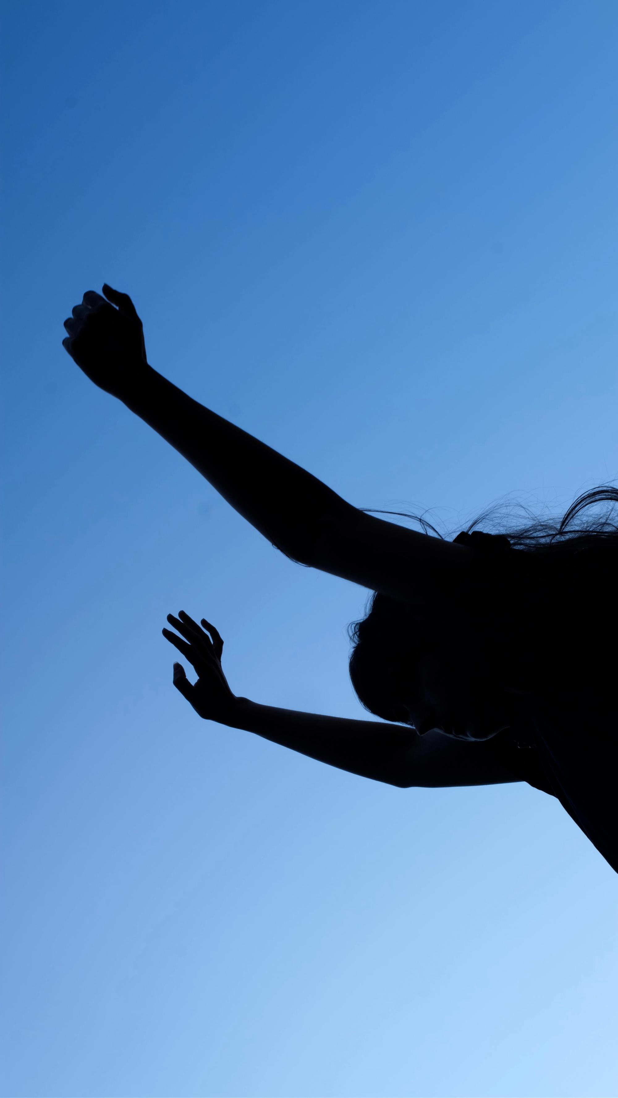 A person reaching their arms ups. The image is rotated so the horizon line is vertical. They are backlit with a blue sky.
