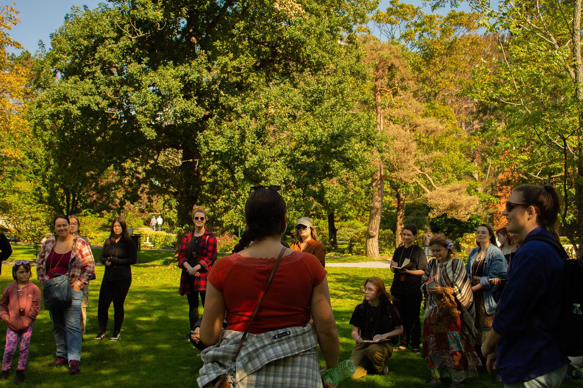 [ID: "Difficult Histories Walk participants at the Halifax Public Gardens gathered in a circle discussing."]