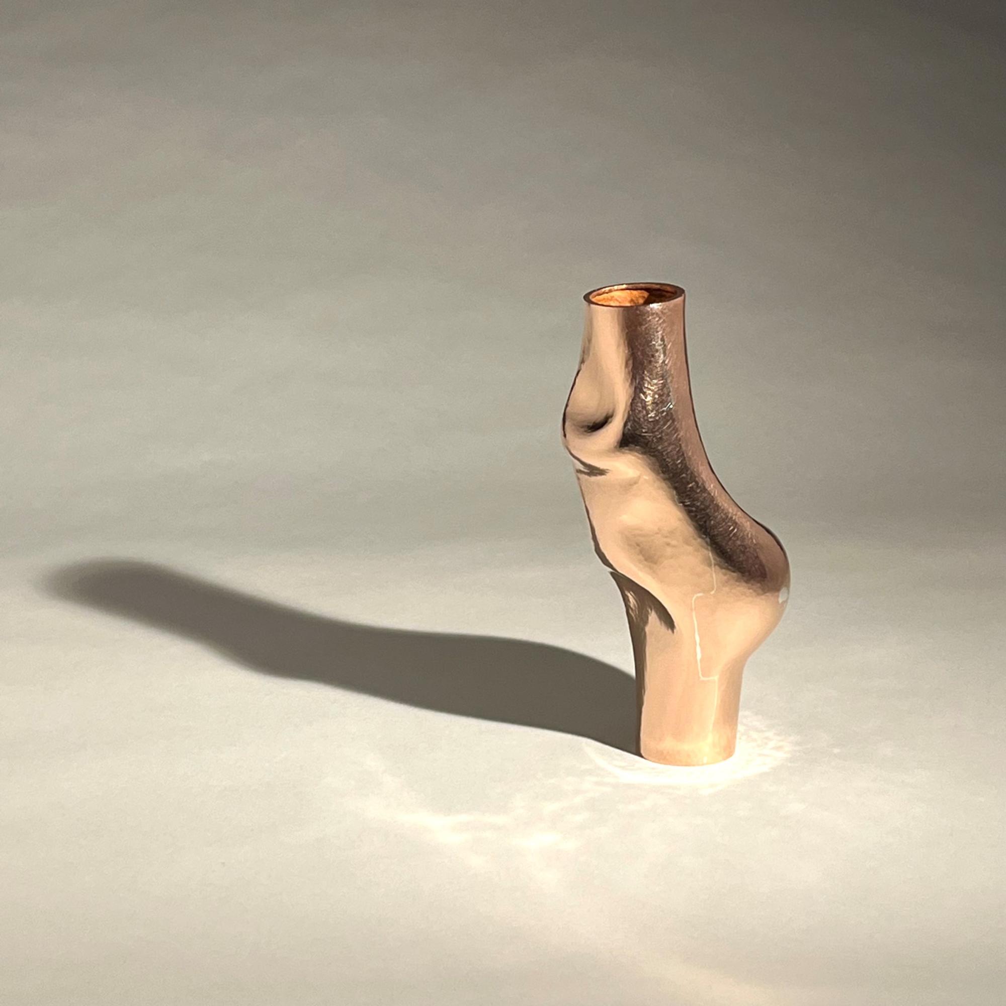 A copper vase. Its shadow is cast to the vases left and there is light being reflected at its base. 