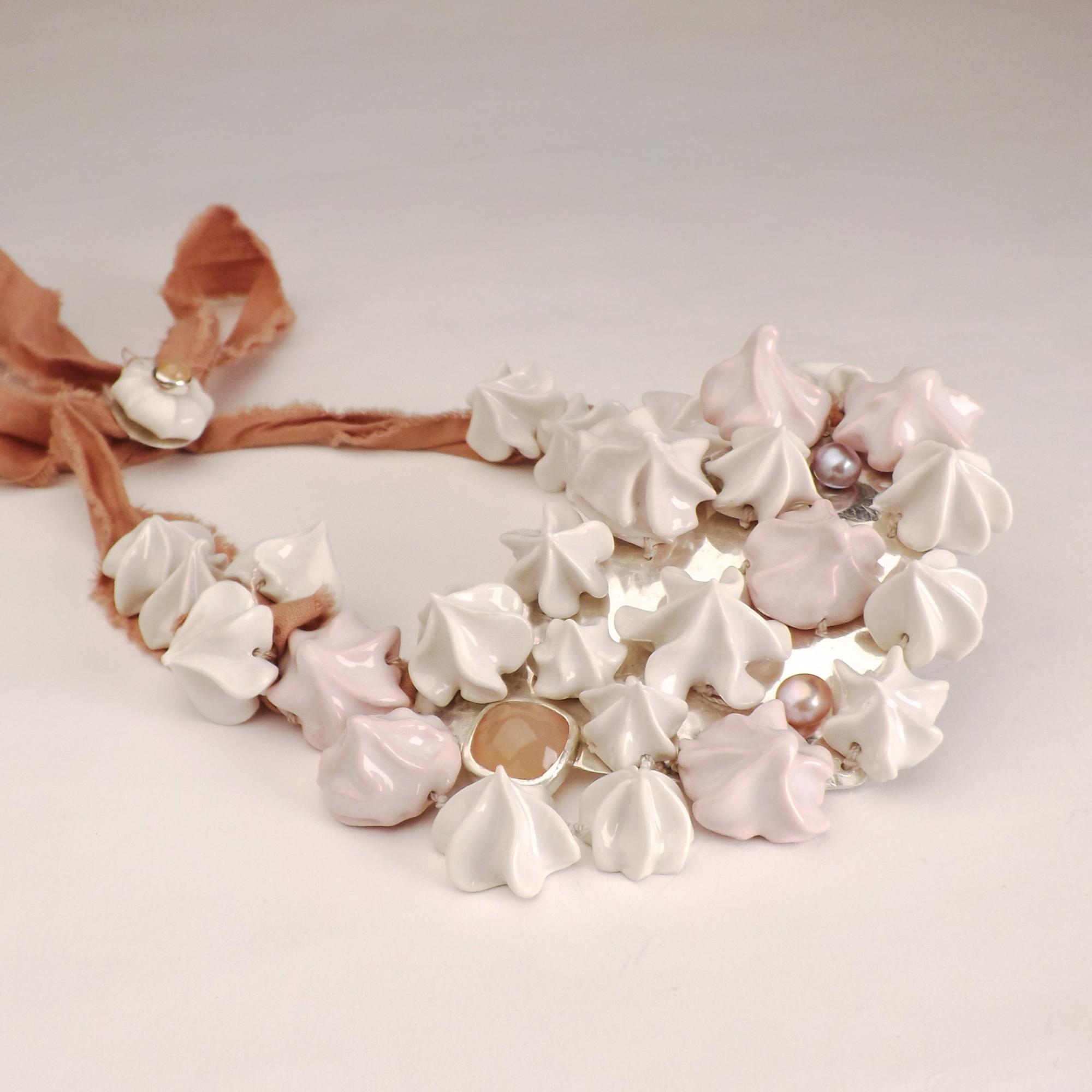 A close-up image of a necklace with white ceramic meringues stitched onto a silver sheet with a square peach moonstone. 