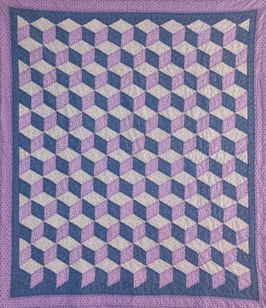 The photo features a close-up of a purple and white checkered cloth. The fabric showcases a distinct pattern, highlighting its lilac hues and textile qualities. It is reminiscent of traditional quilt designs, emphasizing the craftsmanship involved in stitching and needlework.