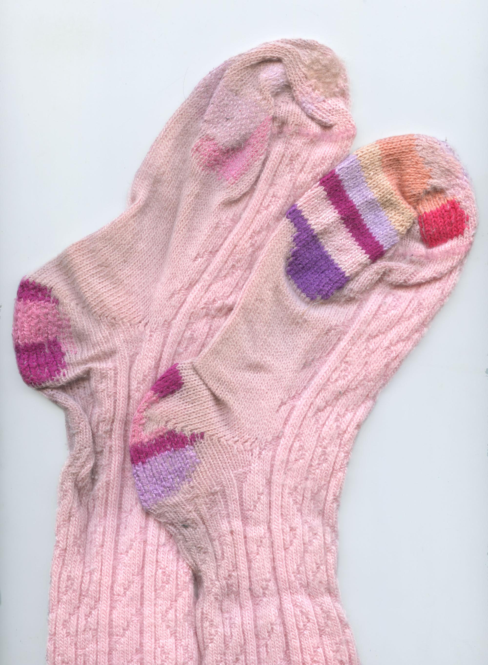 Image of pale pink socks with mending in shades of pink and purple. They are laid flat on their sides and slightly overlap.