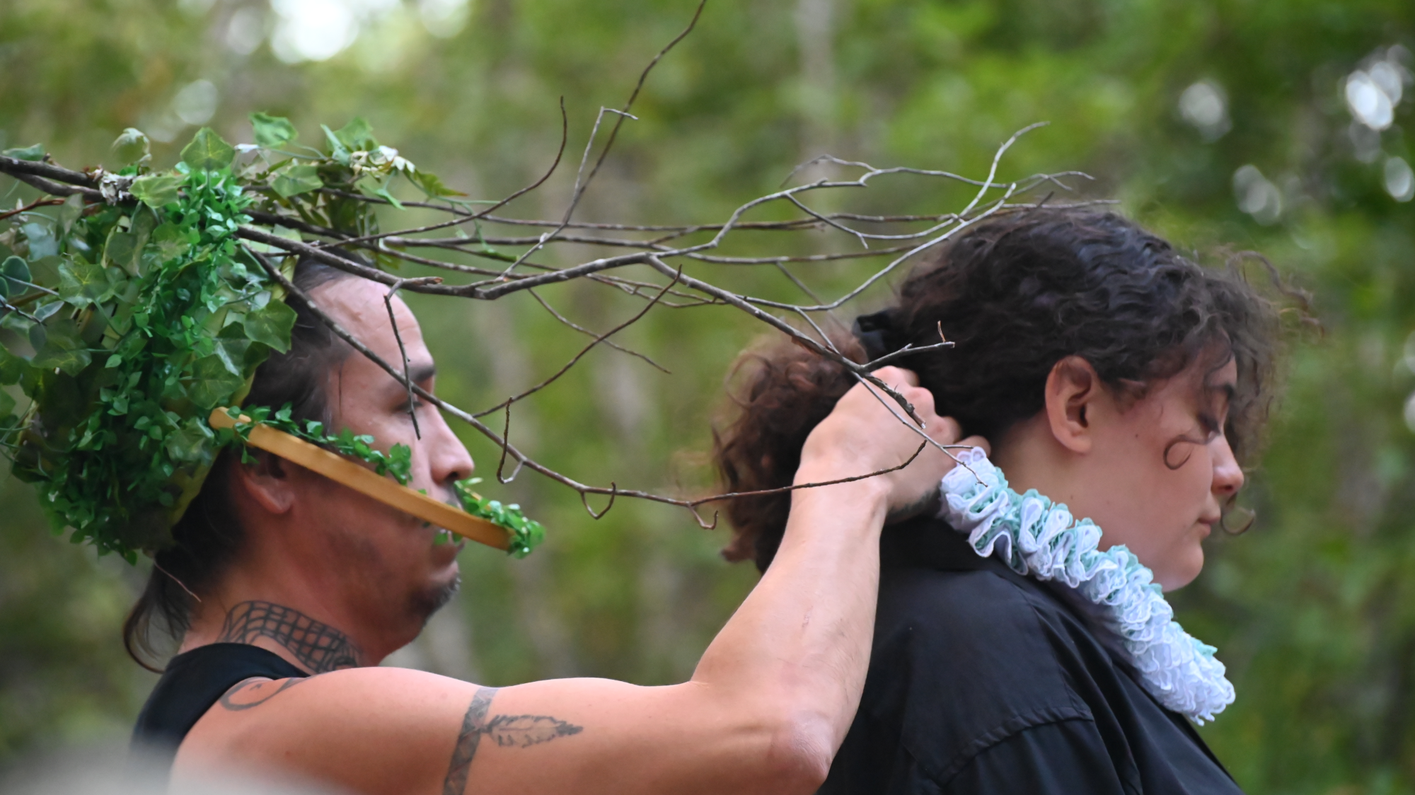 photograph of two performers, Richard "Krow Dog" Taylor, costumed in a basket with leaves and branches and Kayli Raye Marr wearing a lace ruff