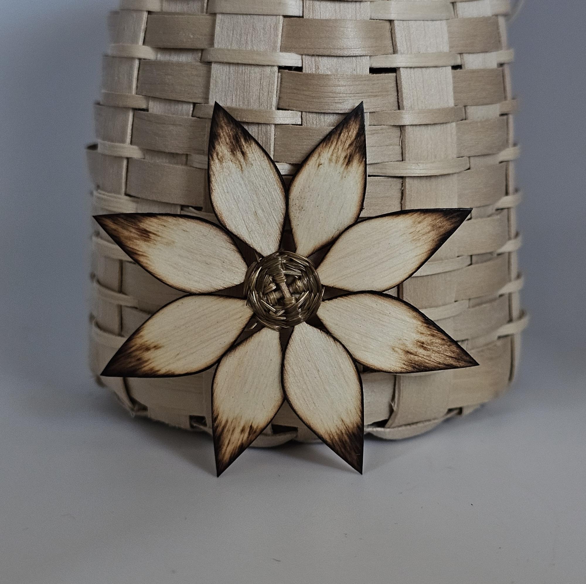 A handcrafted wooden flower with burnt edges, attached to a woven beige basket, showcasing intricate designs and textures.