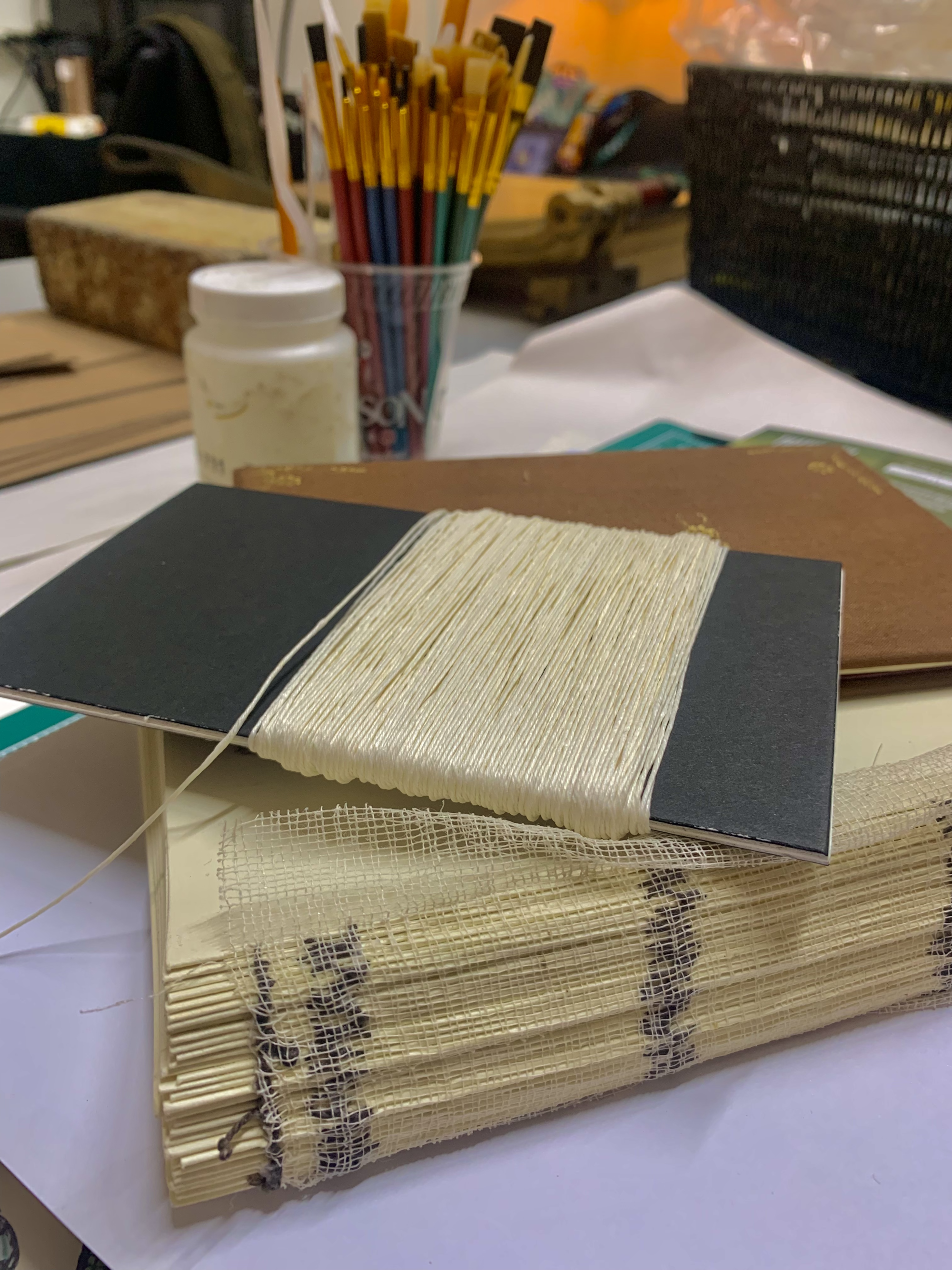 photo of bookbinding supplies—stacked papers, string, glue and paintbrushes