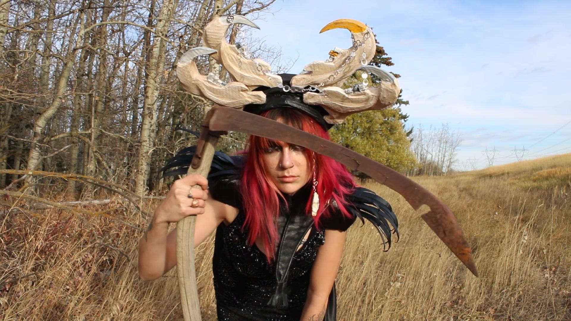 Lydia LeBlanc wearing their piece Jawbone Antlers piece, holding a scythe in a field