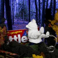 A white miniature bear is on a pedestal surrounded by miniature trees and some normal sized candy.