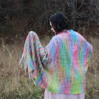 Person stands with rainbow floral shawl facing forest, hand outstretched, looking at part of shawl draped over hand.
