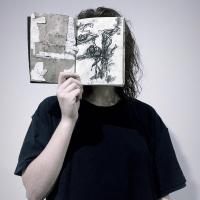 A person holding a book in front of their face, facing out.