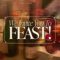 A blurred image of two bottles of wine, glasses, and hands reaching in. White text overlay says "we invite you to feast!"