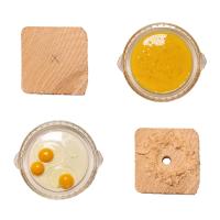 On a white background sits two blocks of wood (one with a drilled hole) and two dishes of eggs (one scrambled). 