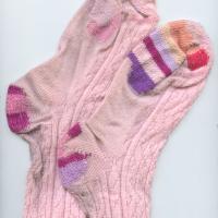Image of pale pink socks with mending in shades of pink and purple. They are laid flat on their sides and slightly overlap.