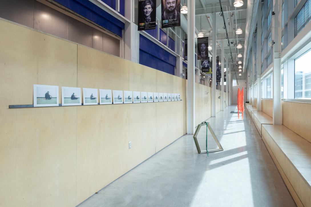 Long hallway gallery with baltic birch walls displaying photos on the wall and geometric sculptures on the floor.