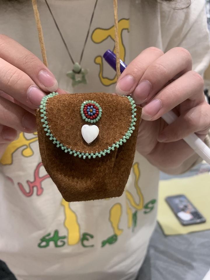 a workshop participant holds their brown leather medicine bag with white heart-shaped shell button and light green edging on the lid